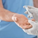 Doctor taking sample of diabetic patient's blood using lancet pen, closeup